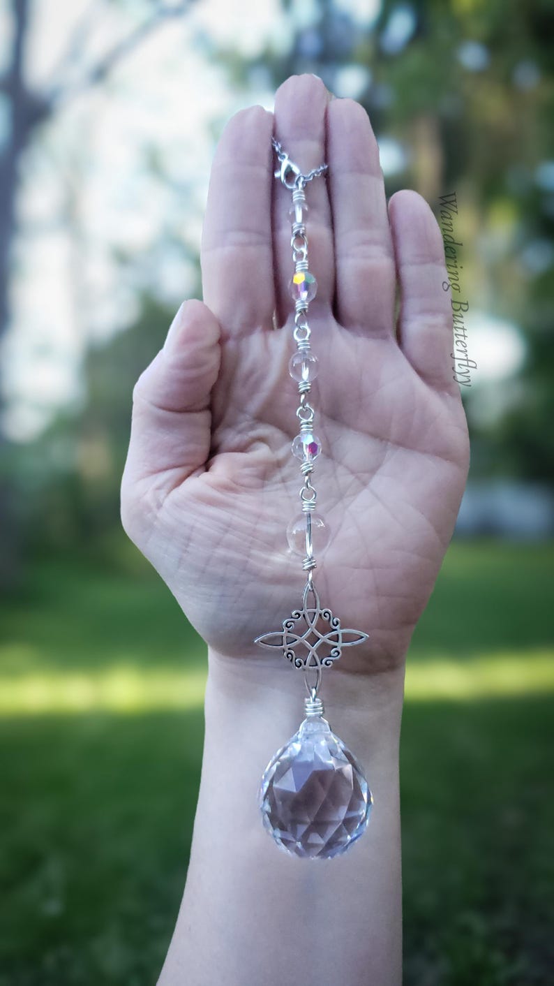 May include: A silver crystal suncatcher with a faceted crystal ball at the base. The suncatcher features clear and iridescent beads, and a decorative cross-shaped charm. The text "Wandering Butterfly" is visible in the background.