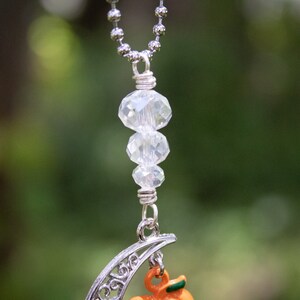 May include: A silver chain necklace with a crescent moon charm and a small orange pumpkin charm. The necklace features three clear crystal beads.