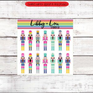 May include: A sheet of 12 colorful nutcracker stickers. The nutcrackers are all wearing different colored hats and have different colored accents. The stickers are from Libby + Lou Sticker Co.