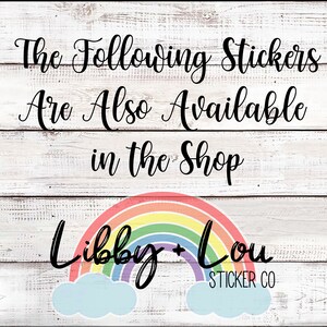 May include: A white wooden sign with black text that reads "The Following Stickers Are Also Available in the Shop". Below the text is a rainbow with clouds and the text "Libby + Lou STICKER CO".
