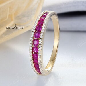 May include: A gold ring with a central row of bright red gemstones, bordered by a row of smaller, clear stones. The ring is displayed against a soft, neutral backdrop, with the brand name "RINGONLY" visible.