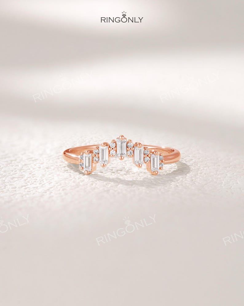 May include: Rose gold ring with a curved design. The ring features a series of rectangular and round-cut clear gemstones. The brand name "RINGONLY" is visible at the top. The ring is set against a white background.