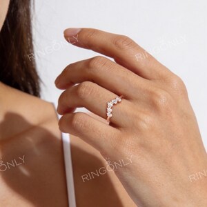 May include: A rose gold ring with a curved design, set with multiple small, clear gemstones. The ring is worn on a finger, with the brand name "RINGONLY" visible in the background.