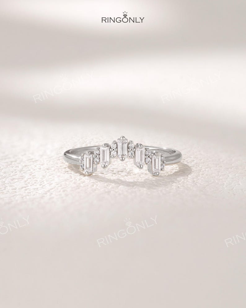 May include: A silver ring with a curved design, featuring rectangular and round-cut gemstones. The ring has a delicate, elegant appearance, with the brand name "RINGONLY" visible at the top.