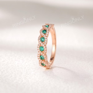 Op de afbeelding: Ros&eacute;gouden ring met een rij smaragdgroene edelstenen afgewisseld met secties van kleine, heldere edelstenen. De ring heeft een delicaat, verweven ontwerp. De merknaam "RINGONLY" is bovenaan zichtbaar.