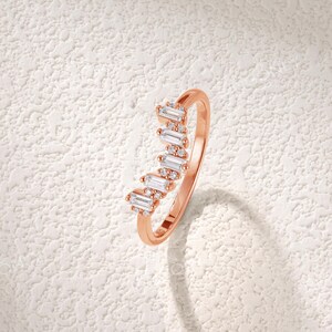 May include: Rose gold ring with a row of baguette-cut and round-cut clear gemstones. The ring has a delicate band and the gemstones are set in a wave-like pattern. The brand name "RINGONLY" is visible in the upper left corner.