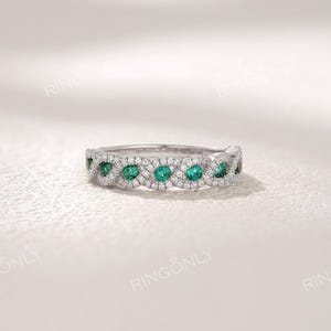 Op de afbeelding: Een zilveren ring met een herhalend patroon van smaragdgroene edelstenen en kleine heldere stenen. De ring is geplaatst tegen een witte achtergrond. De merknaam "RINGONLY" staat bovenaan.