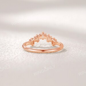 May include: Rose gold ring with a crown-like design. The ring features a delicate band and a detailed, ornate top. The crown design is centered and symmetrical, with small, pointed elements. The ring is set against a soft, white background.