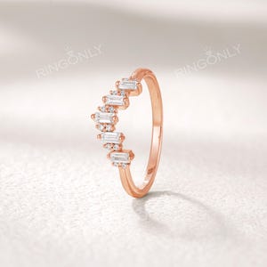 May include: A rose gold ring with a curved design. The ring features a series of rectangular and round-cut white gemstones. The brand name "RINGONLY" is visible at the top of the image.