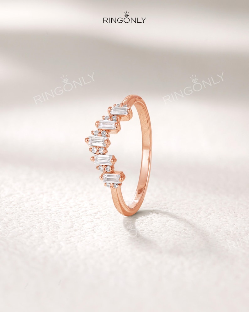 May include: A rose gold ring with a curved design. The ring features a series of rectangular and round-cut white gemstones. The brand name "RINGONLY" is visible at the top of the image.