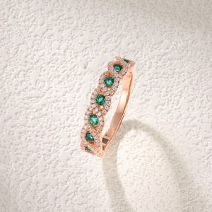 Op de afbeelding: Ros&eacute;gouden ring met smaragdgroene edelstenen en kleine witte diamanten. Het ontwerp van de ring heeft een herhalend patroon van smaragden en diamanten. De merknaam "RINGONLY" is linksboven zichtbaar. Het ontwerp is delicaat.