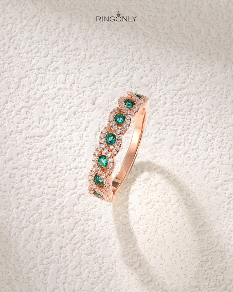 Op de afbeelding: Ros&eacute;gouden ring met smaragdgroene edelstenen en kleine witte diamanten. Het ontwerp van de ring heeft een herhalend patroon van smaragden en diamanten. De merknaam "RINGONLY" is linksboven zichtbaar. Het ontwerp is delicaat.