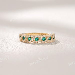 Op de afbeelding: Een gouden ring met een reeks smaragdgroene edelstenen afgewisseld met kleine, heldere edelstenen. De ring heeft een delicaat, sierlijk ontwerp. De merknaam "RINGONLY" is zichtbaar.