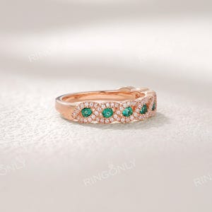 Op de afbeelding: Rosegouden ring met smaragdgroene en heldere edelstenen. De ring heeft een ingewikkeld ontwerp met een gepolijste afwerking. De merknaam "RINGONLY" is bovenaan zichtbaar. Het ontwerp is delicaat en opvallend.