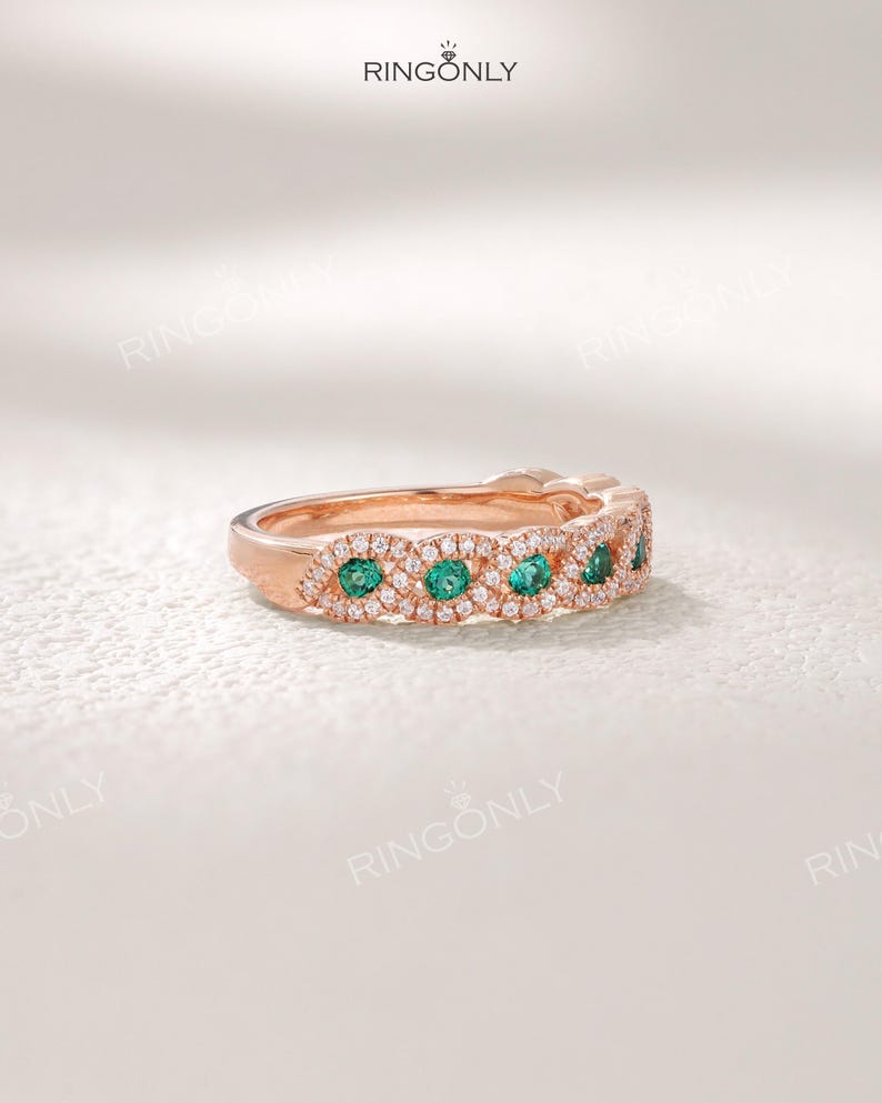 Op de afbeelding: Rosegouden ring met smaragdgroene en heldere edelstenen. De ring heeft een ingewikkeld ontwerp met een gepolijste afwerking. De merknaam "RINGONLY" is bovenaan zichtbaar. Het ontwerp is delicaat en opvallend.