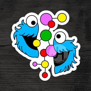 May include: A sticker featuring a blue cartoon character with a large mouth and googly eyes, split in half. A colorful molecular structure is in the center, with red, green, pink, and yellow spheres connected by lines. The sticker has a white border.