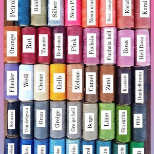 Pu&ograve; includere: Una collezione di 36 bobine di filo in vari colori, tra cui blu, verde, rosso, arancione, giallo, marrone e viola. Le bobine sono etichettate con il nome del colore in tedesco. Il testo "LINHASITA GARN IN 1MM ST&Auml;RKE" &egrave; nella parte superiore dell'immagine.