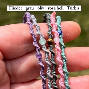 Pu&ograve; includere: Cinque braccialetti intrecciati con cordini e perline di diversi colori. I colori sono viola, grigio, verde oliva, rosa chiaro e turchese. Le perline sono ametista, occhio di tigre, quarzo rosa, acquamarina e lapislazzuli.