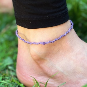 Pu&ograve; includere: Un braccialetto per caviglia viola con un piccolo perno viola al centro.