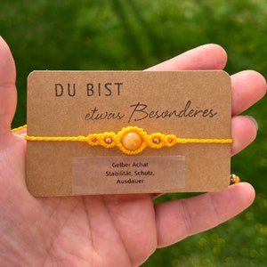 Könnte beinhalten: Gelbes Armband aus Schnur mit einem gelben Achat-Stein und kleinen gelben Blumen-Anhängern. Das Armband liegt auf einer braunen Karte mit dem Text "DU BIST etwas Besonderes" und "Gelber Achat Stabilität, Schutz, Ausdauer".