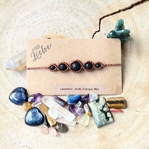 Könnte beinhalten: Ein braunes Armband mit fünf schwarzen Lavasteinen. Das Armband liegt auf einer braunen Karte mit dem Text "mit Liebe" und "Lavastein - Kraft, Energie, Mut".