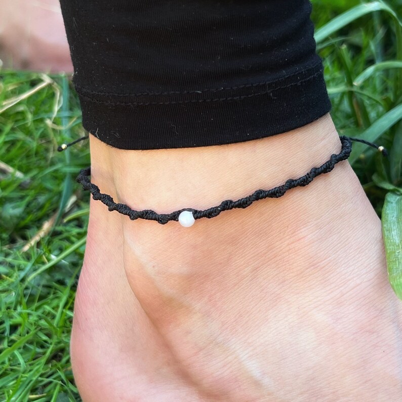 Pu&ograve; includere: Un braccialetto alla caviglia intrecciato nero con un solo perno bianco.