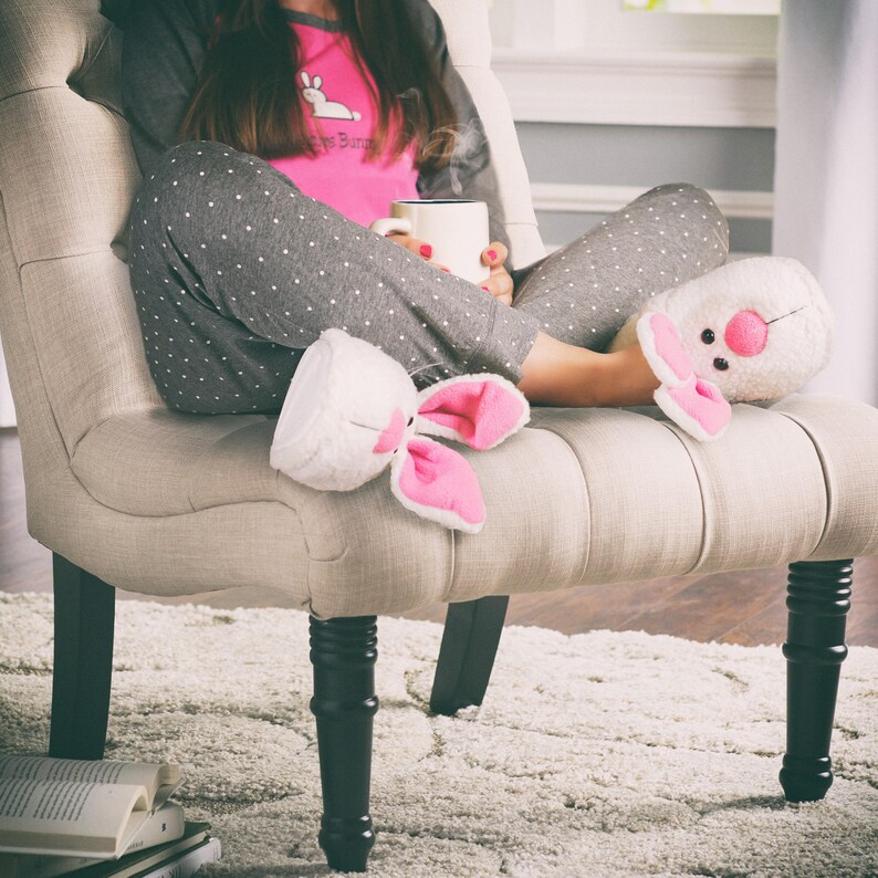 Peut inclure: Une femme portant un pyjama gris et rose avec des pantoufles de lapin blanches est assise dans un fauteuil avec une tasse de caf&eacute; fumant.