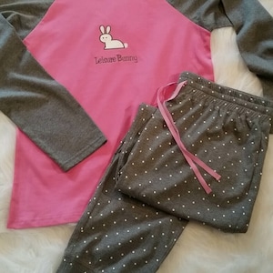 Peut inclure: Un ensemble pyjama rose et gris &agrave; manches longues avec un motif de lapin blanc sur le haut. Le haut est brod&eacute; du texte "Leisure Bunny". Le pantalon a un motif de pois blancs.