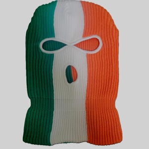 Op de afbeelding: Een gebreide bivakmuts in de kleuren van de Ierse vlag: groen, wit en oranje. De gezichtsopening is wit omlijnd. De bivakmuts is gemaakt van een geribbelde gebreide stof.
