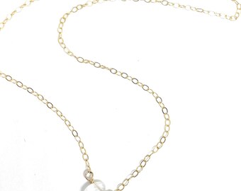 May include: A delicate gold chain necklace featuring a single, small, translucent, teardrop-shaped gemstone pendant suspended from the center. The necklace is constructed with fine, circular gold links that form a continuous, lightweight chain.