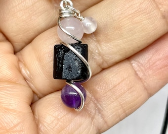 May include: A black obsidian pendant with a pink rose quartz bead and a purple amethyst bead, all wrapped in silver wire and hanging from a black leather cord.