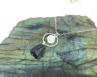 May include: A silver chain necklace with a black tourmaline pendant and a white moonstone bead in a silver circle.