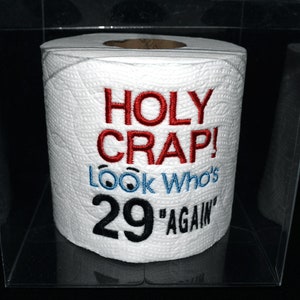May include: A white toilet paper roll with red and black embroidery. The text reads "HOLY CRAP! Look Who's 29 "AGAIN""