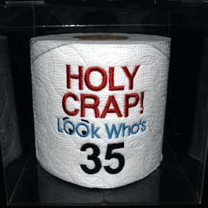 May include: A white toilet paper roll with red and blue embroidery that says "HOLY CRAP! Look Who's 35". The roll is in a clear plastic case.