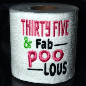 May include: A white toilet paper roll with the text "Thirty Five & Fab-Poo-Lous" embroidered in pink, green, and black.
