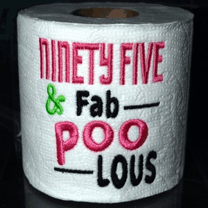 May include: A white toilet paper roll with pink and black embroidery that reads "Ninety Five & Fab-Poo-Lous".