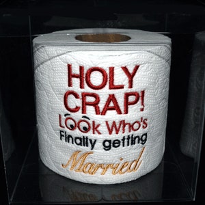 May include: A white toilet paper roll with red embroidery that says "HOLY CRAP! Look Who's Finally Getting Married".
