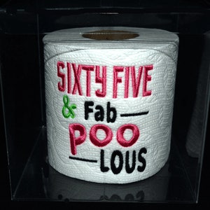 May include: A white toilet paper roll with the text "Sixty Five & Fab-Poo-Lous" embroidered in pink and green.