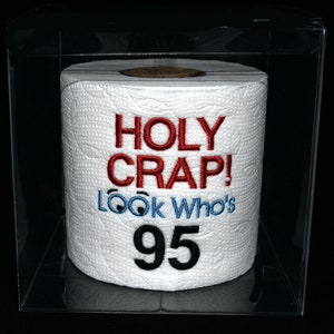 May include: A white toilet paper roll with the text "HOLY CRAP! LOOK WHO'S 95" in red, blue, and black embroidery.
