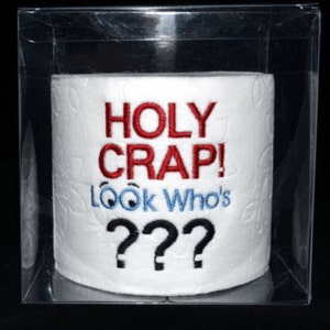 May include: A white toilet paper roll with the text "HOLY CRAP! Look Who's???" embroidered in red, blue, and black.
