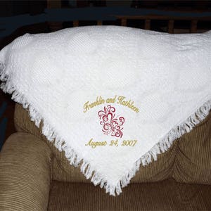 May include: White crocheted throw blanket with a fringed border. The blanket is embroidered with the names "Franklin and Kathleen" and the date "August 24, 2007" in gold thread. A red heart design is embroidered in the center.