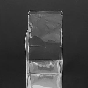 Puede incluir: Un expositor de pl&aacute;stico transparente con tres bolsillos escalonados. El soporte es rectangular con una parte superior plegada y est&aacute; colocado sobre un fondo negro. Los bolsillos est&aacute;n dise&ntilde;ados para guardar y exhibir art&iacute;culos.