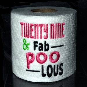 May include: A white toilet paper roll with pink and green embroidery that reads "Twenty Nine & Fab-Poo-Lous".