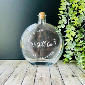 May include: A clear glass bottle with a cork stopper and a white inscription that reads "Rick & Jen We Still Do 2024 St. Maarten".