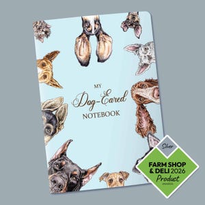 Könnte beinhalten: Ein hellblaues Notizbuch mit dem Text "My Dog-Eared Notebook" und Illustrationen verschiedener Hunderassen. Das Notizbuch hat einen silbernen "Farm Shop & Deli 2026 Product Awards" Aufkleber.