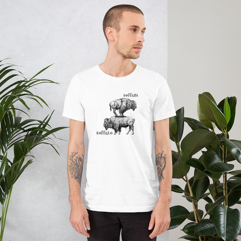 May include: White t-shirt with a black and white illustration of two buffalo stacked on top of each other. The text "Buffalo" is printed below the buffalo and the text "BUFFALO" is printed above the buffalo.