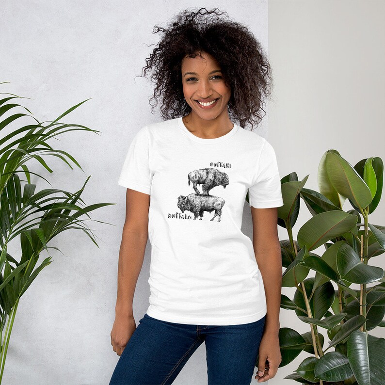May include: A white t-shirt with a black and white illustration of two buffalo stacked on top of each other. The text "Soft as a Buffalo" is above the buffalo and the text "Buffalo" is below the buffalo.