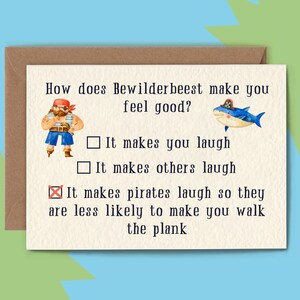 May include: A greeting card with a brown envelope. The card has the text "How does Bewilderbeest make you feel good?" with illustrations of a pirate and a shark. The card's options are "It makes you laugh", "It makes others laugh", and "It makes pirates laugh so they are less likely to make you walk the plank."