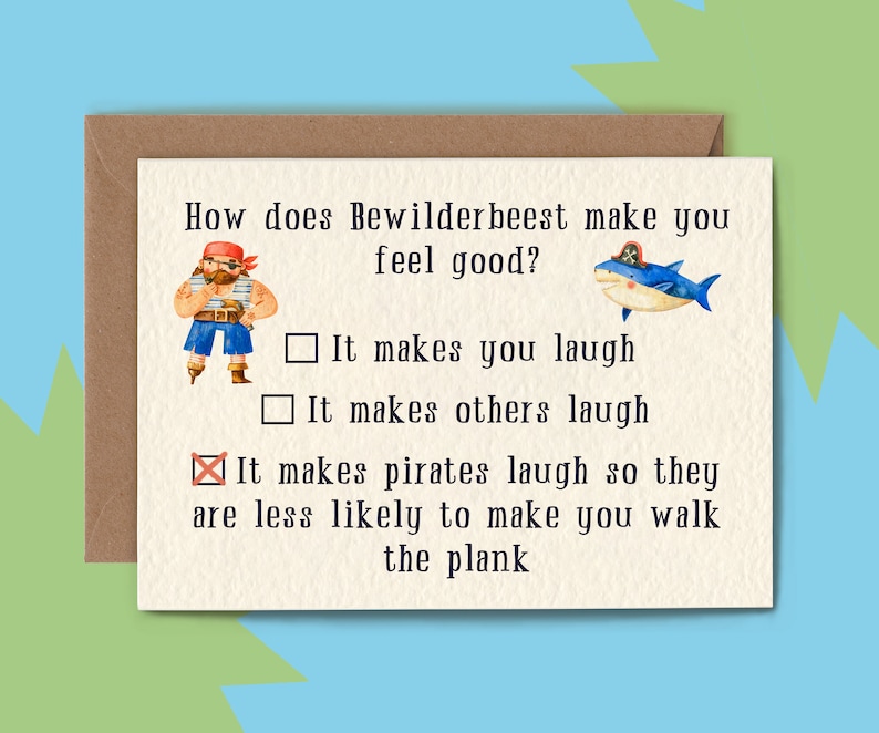 May include: A greeting card with a brown envelope. The card has the text "How does Bewilderbeest make you feel good?" with illustrations of a pirate and a shark. The card's options are "It makes you laugh", "It makes others laugh", and "It makes pirates laugh so they are less likely to make you walk the plank."