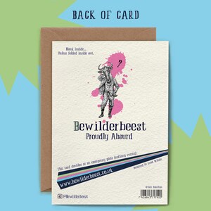 May include: A greeting card with a black and white illustration of a person with a wildebeest head. The card has a pink background with white paint splatters. The text on the card reads "Bewilderbeest Proudly Absurd".